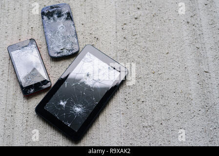 Broken phones and tablet on concrete background. Cracked screen Stock Photo