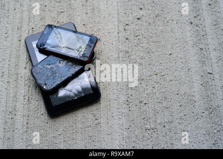 Broken phones and tablet on concrete background. Cracked screen Stock Photo