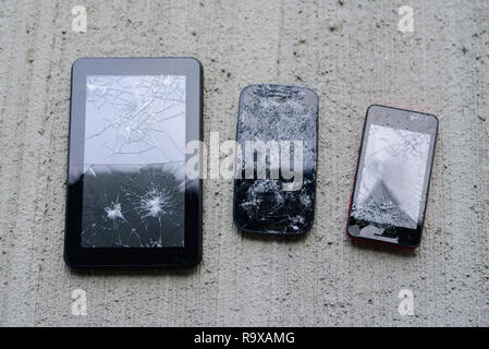 Broken phones and tablet on concrete background. Cracked screen Stock Photo