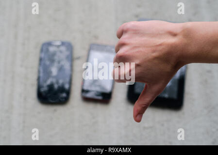 Thumbs down hand with broken phones and tablet on concrete background Stock Photo