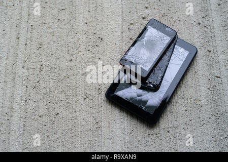 Broken phones and tablet on concrete background. Cracked screen Stock Photo