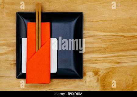 Black ceramic bowls  and bamboo chopsticks for sushi food with orange napkin. Stock Photo