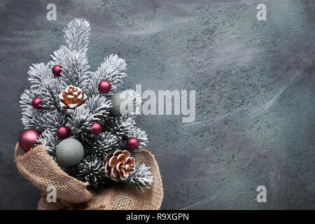 Small Christmas tree in sackcloth decorated with red baubles and berries on dark textured background with copy-space Stock Photo