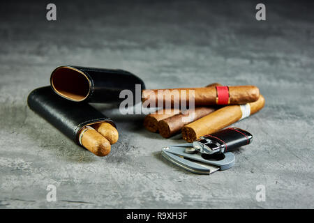 Six Cuban cigars on a stone table with a lighter, cutter and a leather case. Stock Photo