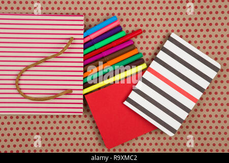 Education and celebratory concept - handmade striped shopping bag, gift bags, desk accessories, colored felt-tip pens, red and striped notepads on cra Stock Photo