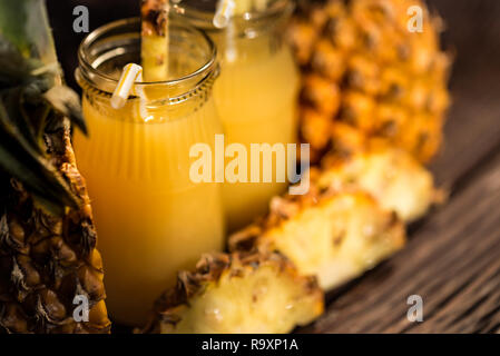 Jars of pulpy fresh pineapple juice and pineapple slices placed on a wooden table. Summer drink concept Stock Photo