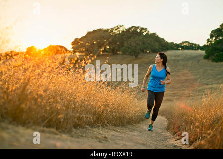 Mid adult woman running on a trail through a grassy field. Stock Photo