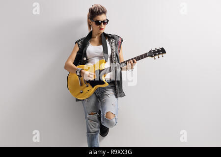 Female punker in a leather vest leaning on a wall and playing a guitar Stock Photo