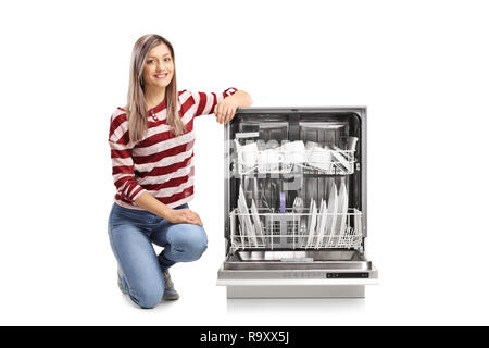 Beautiful young woman kneeling next to an open dishwasher isolated on white background Stock Photo