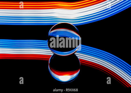 Light painting with a lens ball / crystal ball / glass ball / sphere with colorful blue striped reflections on black surface. Stock Photo