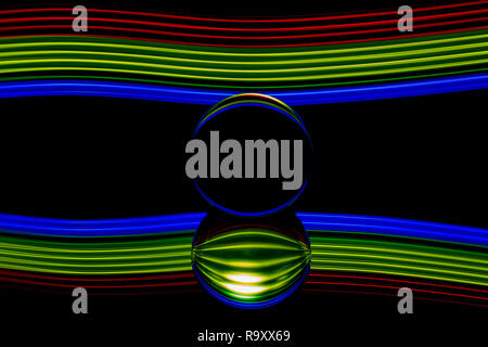 Light painting with a lens ball / crystal ball / glass ball / sphere with colorful blue striped reflections on black surface. Copy Space on black. Stock Photo
