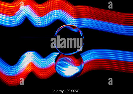 Light painting with a lens ball / crystal ball / glass ball / sphere with colorful blue striped reflections on black surface. Stock Photo