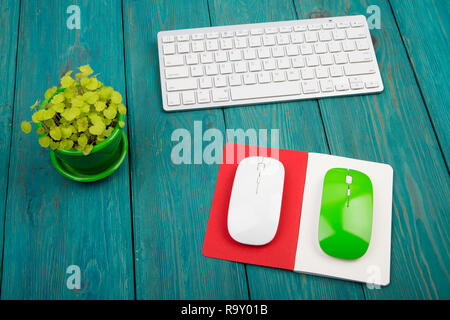 Wireless slim white keyboard, green and white mouses, notepad, flower on blue wooden background Stock Photo
