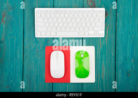 Wireless slim white keyboard, green and white mouses, notepad on blue wooden background Stock Photo