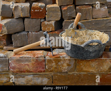Masonry stone wall construction with mortar and brick hammer trowel tools DIY Stock Photo