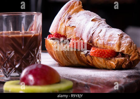 Croissant with chocolate cream and strawberry on the black marble plate. Stock Photo