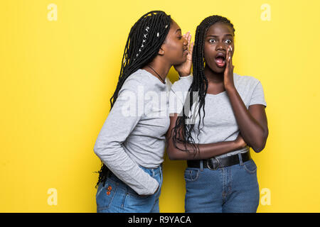 Portrait of two young african women sharing secrets isolated over yellow background Stock Photo