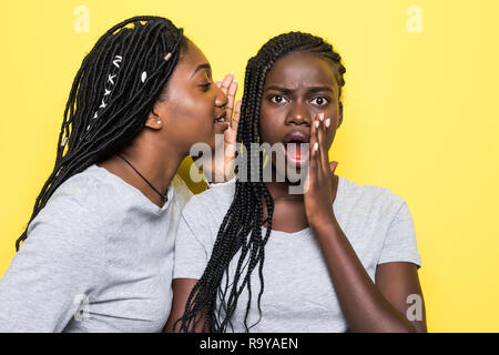 Portrait of two young african women sharing secrets isolated over yellow background Stock Photo