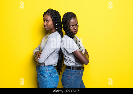 Portriat of two african women standing with arms crossed after quarrel isolated over yellow background Stock Photo