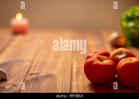 Rustic kitchen table, some tomatoes in the foreground and in the background some foods out of focus. Resource for designers.
