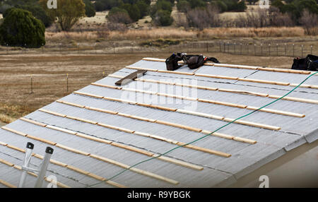 Wooden slats laying on rooftop with tool belt and clay tile in preparation for roofing Stock Photo