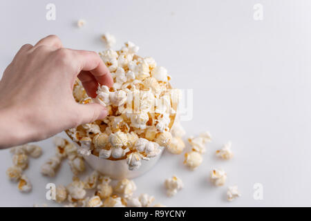 A hand is taking a popcorn from a paper bucket on a white background. Top view. Close-up. Stock Photo