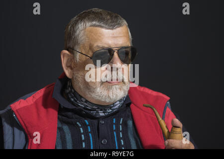 Nice low key portrait of senior man in black eyeglasses holding tobacco-pipe Stock Photo