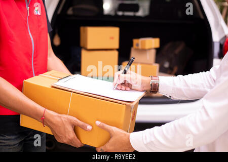 Asian young man and delivery worker are signing documents for send parcels, cardboard boxes in the background - Image Stock Photo