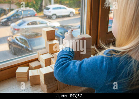Child playing with wooden blocks or cubes at home by the window, educational toys concept. Development of kids fine motor skills, imagination, logical Stock Photo