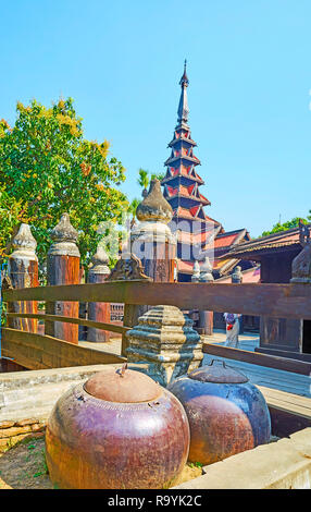 The large donation bowls in front of the fence of the medieval wooden Bagaya Monastery, Ava (Inwa), Myanmar. Stock Photo