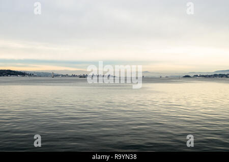 Thin Oslofjord coastline with two local ferry boats and two white lighthouses in winter calm sunset. Stock Photo