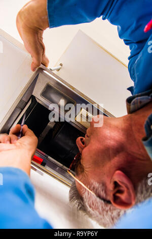 Mature repairman is fixing the kitchen vent hood installation with screwdriver Stock Photo