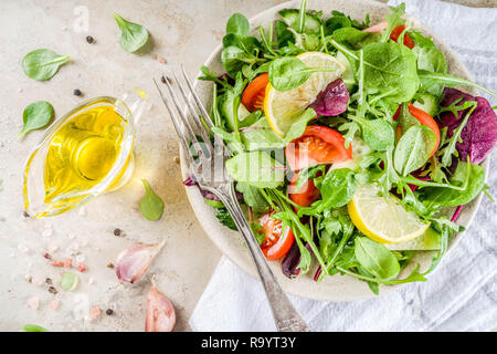 Fresh spring detox mix salad with vegetables (cucumber, lemon, tomato, arugula, and baby spinach), on light slate, stone or concrete background. Top v Stock Photo