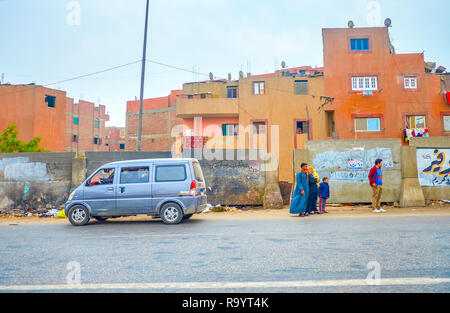 CAIRO, EGYPT - DECEMBER 20, 2017: The egyptian family wait for the transport at the edge of the road in poor residential neighborhood of Cairo, on Dec Stock Photo