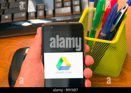 PIATRA NEAMT, ROMANIA - JULY 30, 2018: Hand holds a mobile phone with Google drive logo on the screen, office background. Stock Photo