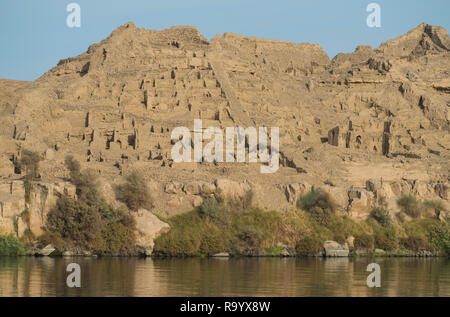 View from the Nile River of ancient egyptian town ruins on mountainside in Aswan Egypt Stock Photo