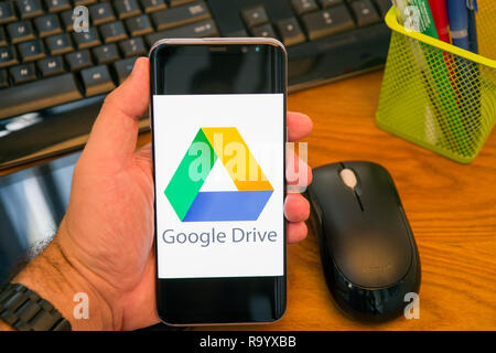 PIATRA NEAMT, ROMANIA - JULY 30, 2018: Hand holds a Samsung S8+ with Google drive logo on the screen, office background. Stock Photo