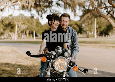 Precious Cute Leisure Lifestyle Portrait of Handsome Guy and Girl Beauty Being Silly Fun and Laughing while Riding Classic Motorcycle Bike in Love Stock Photo