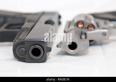 Two handguns, a black 9mm pistol and a silver 357 magnum revolver, loaded with gold hollow point bullets side by side on a white background Stock Photo