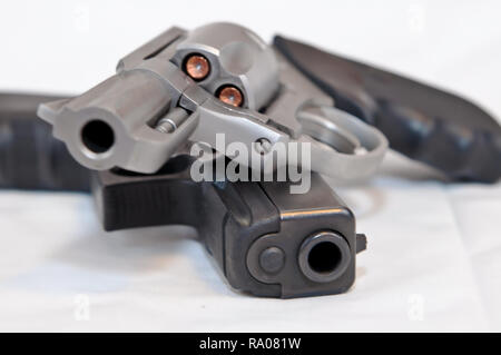 Two handguns, a silver 357 magnum revolver on top of a black 9mm pistol on a white background. The revolver is shown loaded with hollow point bullets Stock Photo