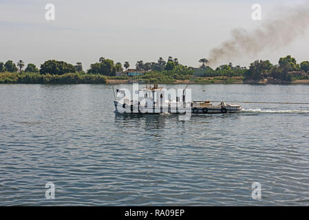 Small tug boat towing a barge on nile river in Egypt through rural countryside landscape with exhaust smoke fumes Stock Photo