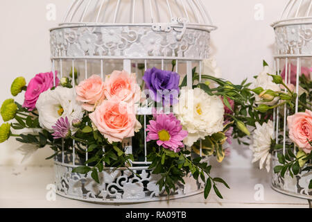 Various bridal flower heads in vintage ornate bird cage as bloom decoration at a wedding reception. Stock Photo