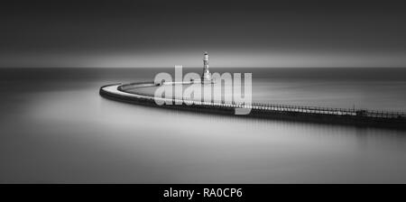 A moody Fine Art black & white long exposure of Roker Pier at sunset with the long sweeping path giving a soft mirror reflection in the North Sea Stock Photo