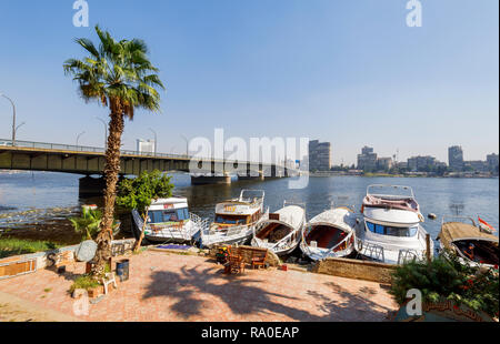 Boats moored on the riverbank by Cairo University Bridge spanning the River Nile in Giza, Cairo, Egypt, looking towards the east bank on a sunny day Stock Photo