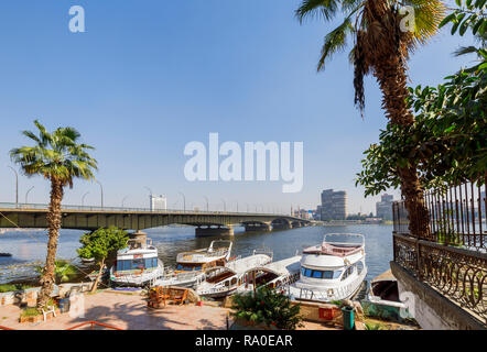 Boats moored on the riverbank by Cairo University Bridge spanning the River Nile in Giza, Cairo, Egypt, looking towards the east bank on a sunny day Stock Photo