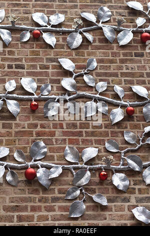 Tree of life decorated with red balls against a red brick wall Stock Photo