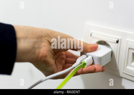Charger with two cables in the socket and female hand holding it, closeup shot Stock Photo