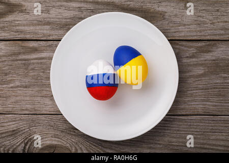 Two Easter eggs painted in the color of the flags of Russia and Ukraine in a ceramic plate on a wooden table, top view Stock Photo