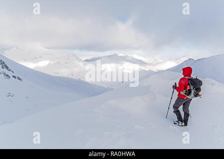 Female hiker in Red jacket looking over snow covered mountains in the Mamores Mountain range in the highlands of Scotland during winter. Stock Photo