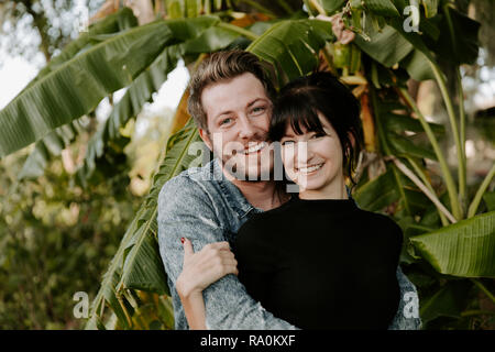 Portrait of Two Cute Modern Caucasian Beautiful Young Adult Guy Boyfriend Lady Girlfriend Couple Hugging and Kissing in Love, Nature with Green Plants Stock Photo